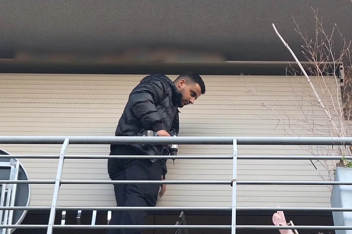 Technicien, visseuse en main, devant le tablier entièrement descendu d'un volet roulant, sur un balcon au deuxième étage.